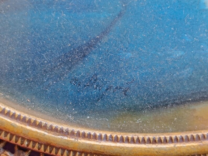 K&ouml;nnte beinhalten: Nahaufnahme eines Miniaturgem&auml;ldes im Vintage-Stil mit blau-wei&szlig;em Hintergrund. Das Gem&auml;lde ist in einem goldfarbenen, verzierten ovalen Rahmen gerahmt. Die Signatur des K&uuml;nstlers ist unten in der Mitte des Gem&auml;ldes zu sehen.