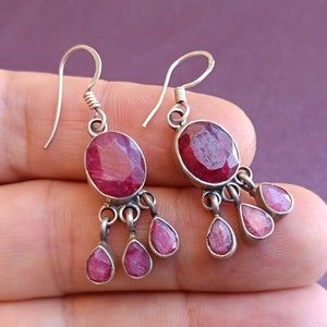 May include: A pair of silver dangle earrings with pink oval-shaped gemstones. The earrings have three smaller pink gemstones hanging from the larger gemstone.
