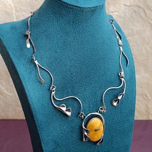 May include: A silver necklace with a large amber pendant. The necklace features a delicate, flowing design with leaf-like accents.