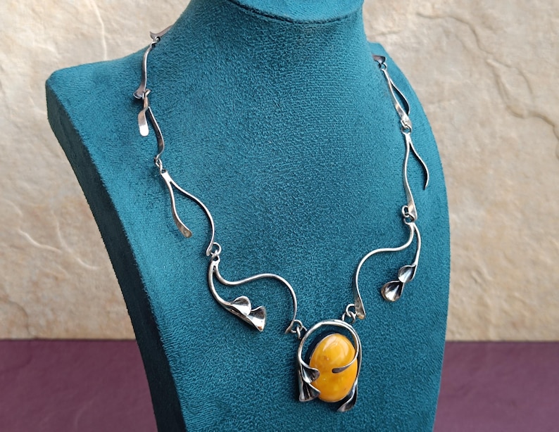 May include: A silver necklace with a large amber pendant. The necklace features a delicate, flowing design with leaf-like accents.
