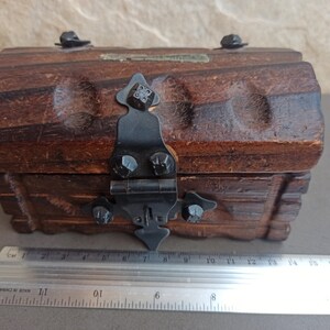May include: A small wooden treasure chest with a hinged lid and a black metal latch. The chest has a carved design and is made of dark brown wood.