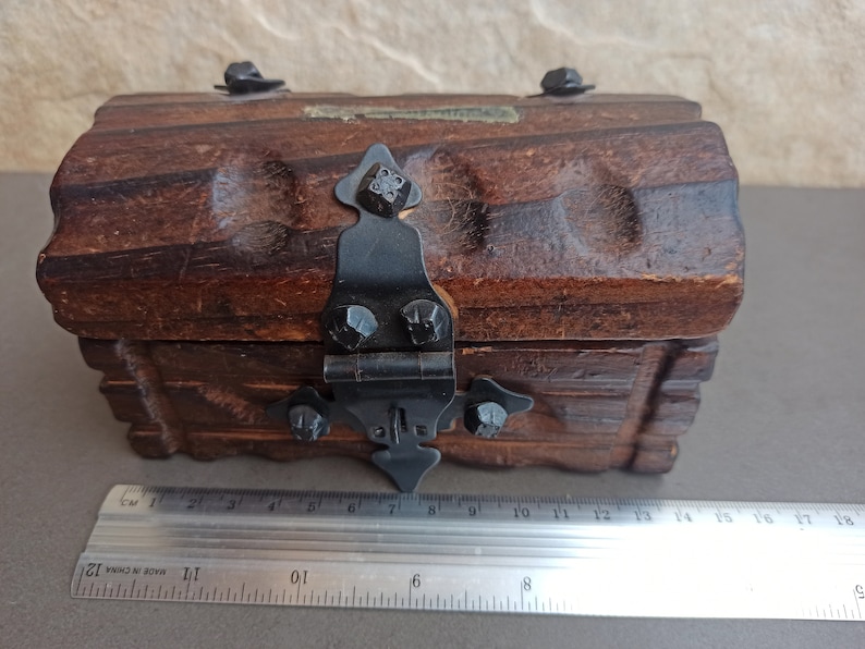 May include: A small wooden treasure chest with a hinged lid and a black metal latch. The chest has a carved design and is made of dark brown wood.