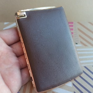 May include: A brown leather cigarette case with a silver hinge and a gold-colored metal clasp.
