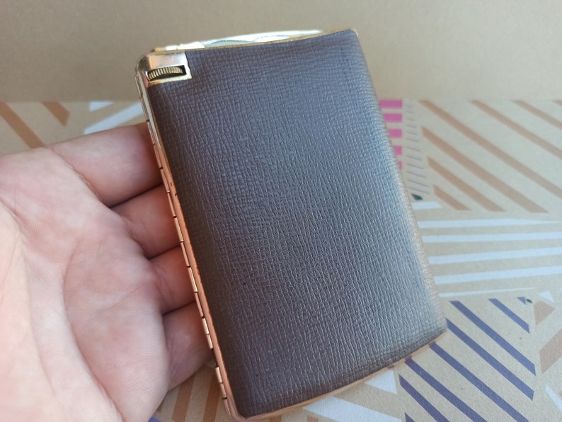 May include: A brown leather cigarette case with a silver hinge and a gold-colored metal clasp.