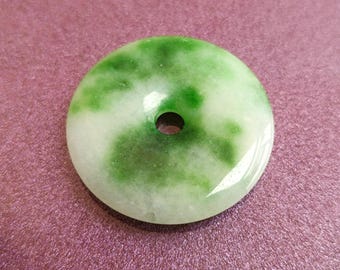 May include: A round jade pendant with a central hole. The pendant features a marbled pattern of green and white, with a polished, glossy finish. The jade is a natural stone, and the pendant is likely used for jewelry or decorative purposes.