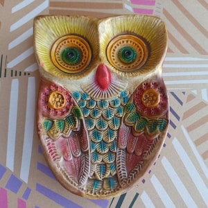 May include: A colorful ceramic owl dish with a red beak, blue and green feathers, and yellow eyes. The owl is decorated with floral patterns in shades of red, yellow, and green.