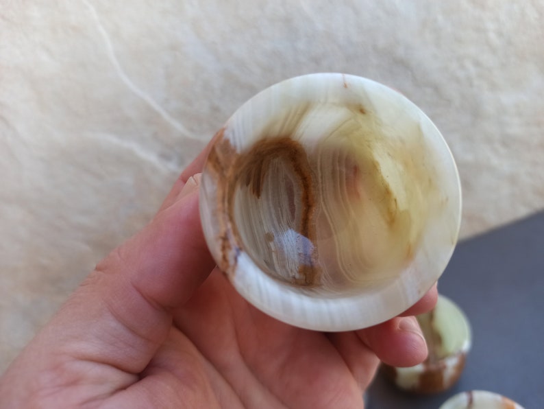 K&ouml;nnte beinhalten: Eine kleine, wei&szlig;e, gr&uuml;ne und braune Onyxschale mit einer glatten, polierten Oberfl&auml;che. Die Schale ist aus Naturstein gefertigt und hat ein einzigartiges, wirbelndes Muster.