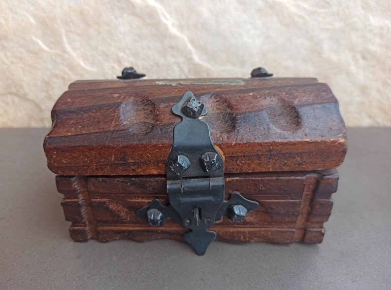 May include: A small wooden treasure chest with a black metal hinge and clasp. The chest has a carved design and is closed.