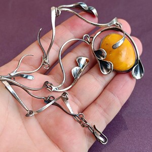 May include: A silver necklace with a large amber stone pendant. The pendant is surrounded by silver leaves and the chain is made of silver links.