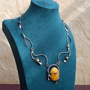 May include: A silver necklace with a large amber stone pendant. The necklace is made of twisted wire and has a delicate floral design.