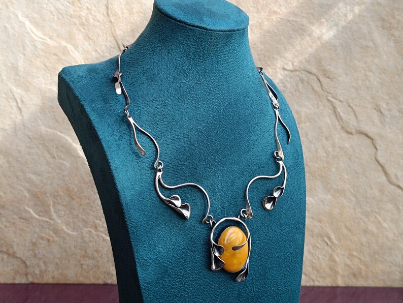 May include: A silver necklace with a large amber stone pendant. The necklace is made of twisted wire and has a delicate floral design.