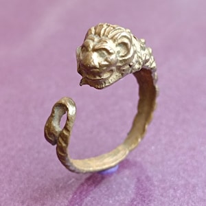 May include: A gold-toned ring with a lion's head design. The ring is made of metal and has a simple band.
