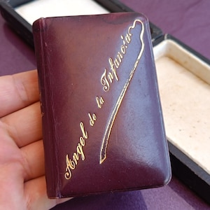 Peut inclure: Un petit livre relié en cuir bordeaux avec une inscription dorée qui dit "Angel de la Infancia".