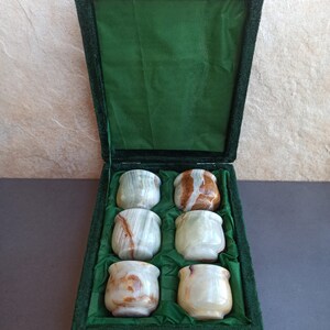 K&ouml;nnte beinhalten: Ein Set mit sechs gr&uuml;nen und braunen Onyx-Schnapsgl&auml;sern in einer gr&uuml;nen Samtbox. Die Gl&auml;ser sind in zwei Reihen mit je drei Gl&auml;sern angeordnet.