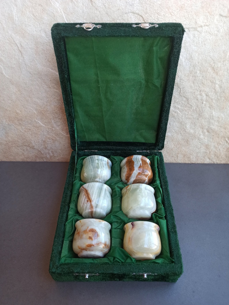 K&ouml;nnte beinhalten: Ein Set mit sechs gr&uuml;nen und braunen Onyx-Schnapsgl&auml;sern in einer gr&uuml;nen Samtbox. Die Gl&auml;ser sind in zwei Reihen mit je drei Gl&auml;sern angeordnet.