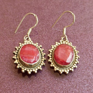 Può includere: Un paio di orecchini d'argento con gocce ovali di pietre preziose rosse. Gli orecchini hanno un design in argento dettagliato attorno alle pietre.