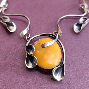 May include: A silver necklace with a large amber pendant. The pendant is surrounded by silver leaves and swirls.
