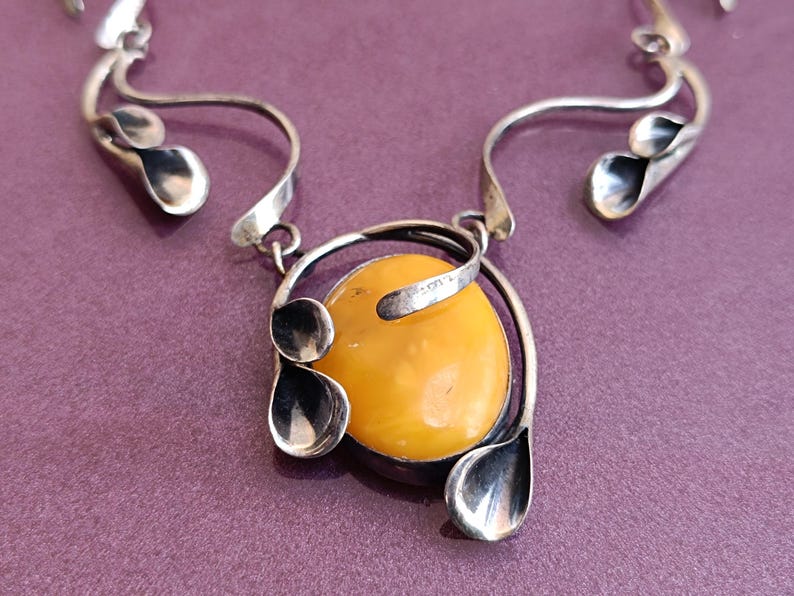 May include: A silver necklace with a large amber pendant. The pendant is surrounded by silver leaves and swirls.