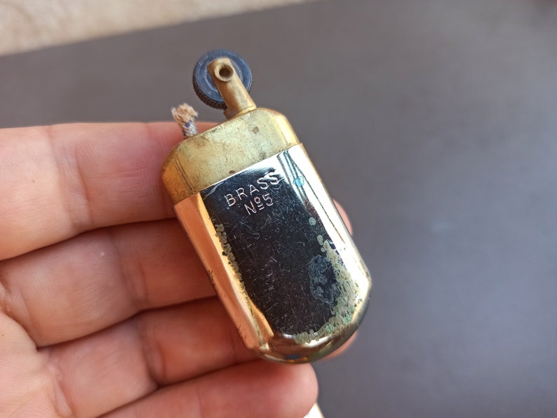 May include: A vintage brass lighter with a silver finish. The lighter has a wick and a flint wheel. The lighter is engraved with the words "BRASS N95".