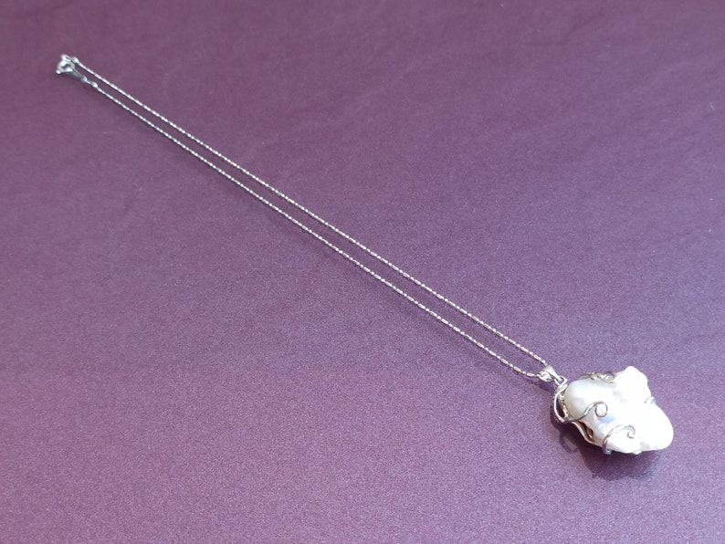 May include: A silver chain necklace with a white pearl pendant wrapped in silver wire.