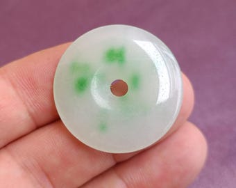 May include: A white jade pendant with a hole in the center and green jade inclusions. The pendant is round and has a smooth surface.