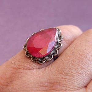 Pode incluir: Um anel de prata com uma grande pedra vermelha em forma de l&aacute;grima.