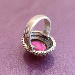 Op de afbeelding: Een zilveren ring met een roze ovale edelsteen gezet in een zilveren bezel. De ring heeft een gedetailleerde band met een textuur.