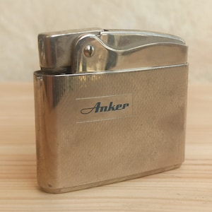 May include: Silver lighter with a textured finish and the word "Anker" printed on the front.