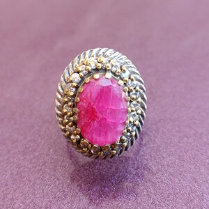 Op de afbeelding: Een zilveren ring met een roze edelsteen omringd door kleinere witte edelstenen. De ring heeft een getextureerde band.