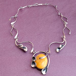 May include: A silver necklace with a large amber pendant. The pendant is surrounded by silver leaves and the chain is made of delicate silver links.
