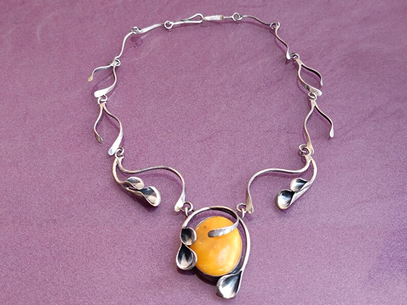 May include: A silver necklace with a large amber pendant. The pendant is surrounded by silver leaves and the chain is made of delicate silver links.