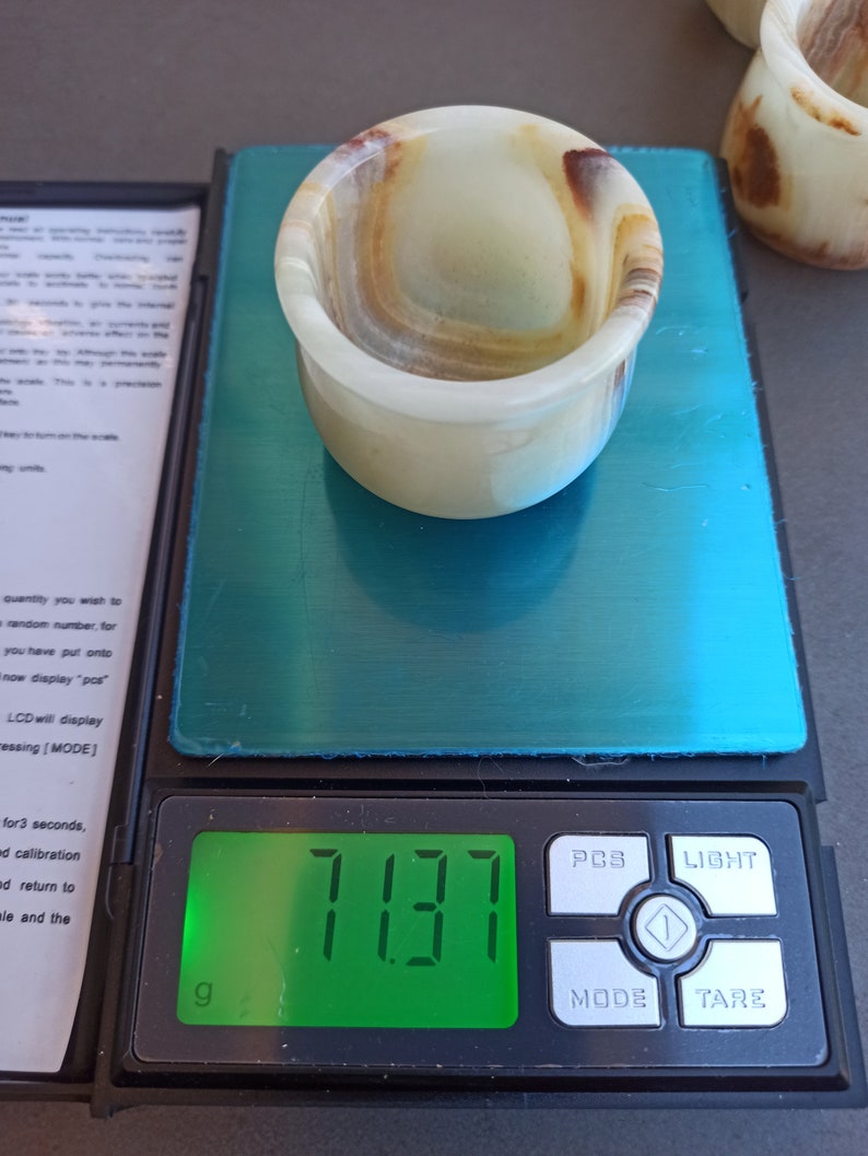 K&ouml;nnte beinhalten: Ein wei&szlig;es und braunes Onyx-Schnapsglas mit einem Gewicht von 7,137 Gramm auf einer digitalen Waage.