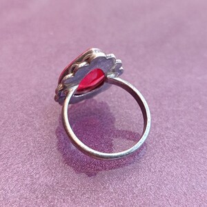 Pode incluir: Um anel de prata com uma gema vermelha engastada em um design decorativo e ornamentado.