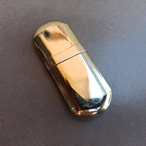 May include: A silver metal lighter case with a rounded shape.
