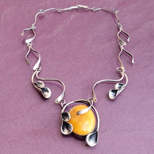 May include: A silver necklace with a large amber pendant. The pendant is surrounded by silver leaves and the necklace is made of a series of silver loops.