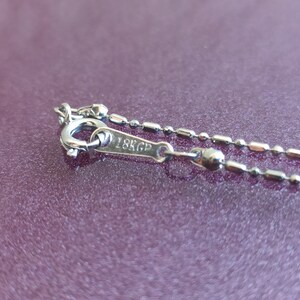 May include: Close-up of a silver chain necklace with a clasp that reads "18K GP".