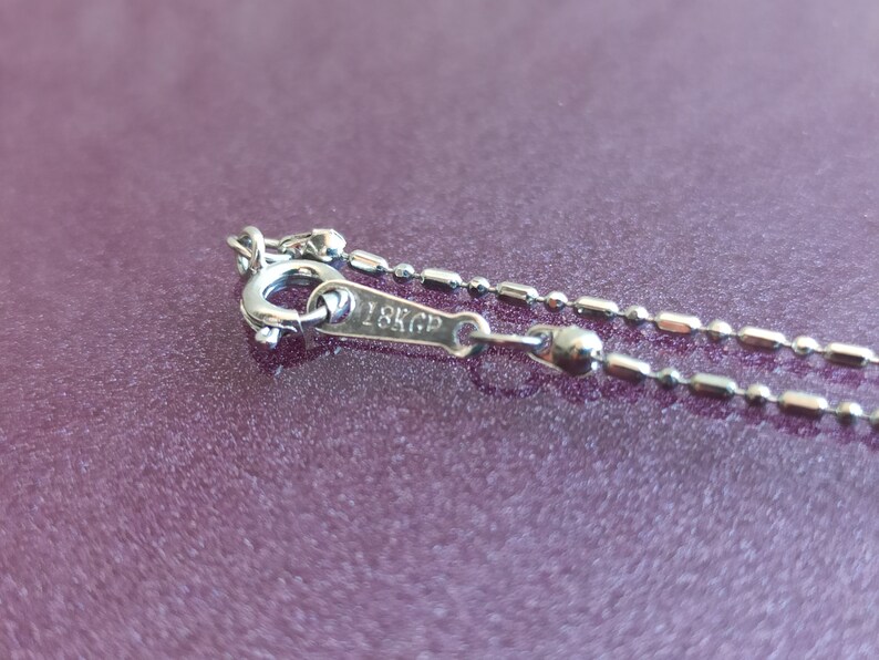 May include: Close-up of a silver chain necklace with a clasp that reads "18K GP".
