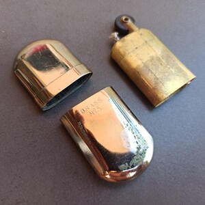 May include: A vintage brass lighter with a hinged lid and a small, round knob on the top. The lighter is engraved with the words "BRASS NO. 5".