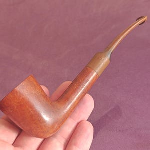 May include: A brown wooden smoking pipe with a curved stem. The pipe is made of a dark wood with a smooth finish.