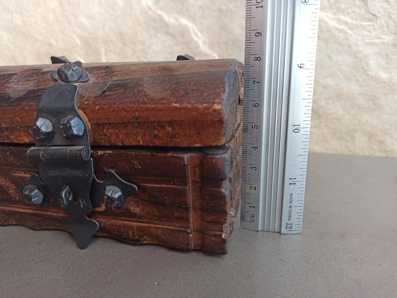 May include: A wooden box with a hinged lid and a metal latch. The box is decorated with carved details and has a dark brown finish.