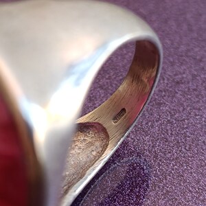 Peut inclure: Gros plan de l'int&eacute;rieur d'une bague en argent avec une pierre rouge. La bague a une finition lisse et polie et un design simple.
