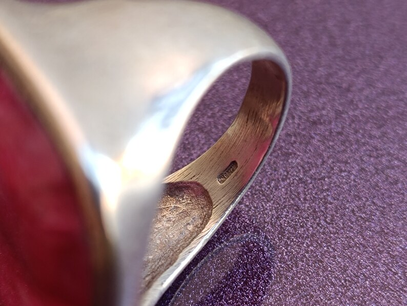 Peut inclure: Gros plan de l'int&eacute;rieur d'une bague en argent avec une pierre rouge. La bague a une finition lisse et polie et un design simple.