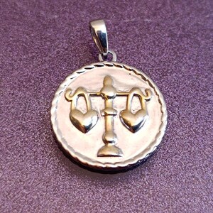 Può includere: Ciondolo color argento raffigurante il segno zodiacale della Bilancia. Il ciondolo circolare ha un bordo strutturato. Il simbolo della Bilancia è una bilancia con pesi a forma di cuore. Su sfondo viola strutturato.