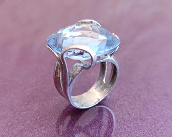 May include: A silver ring with a large, light blue gemstone. The ring has a delicate, organic design.