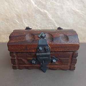 May include: A small wooden treasure chest with a black metal hinge and clasp. The chest has a carved design on the front and sides.