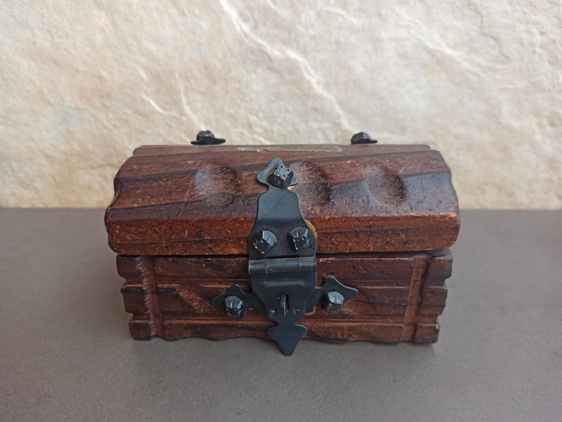 May include: A small wooden treasure chest with a black metal hinge and clasp. The chest has a carved design on the front and sides.