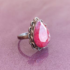 Pode incluir: Um anel de prata com uma gema rosa em forma de l&aacute;grima engastada em uma moldura de prata decorativa.