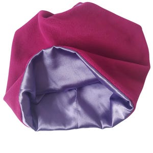 Könnte beinhalten: Eine Schlafhaube aus fuchsia-rosa Satin. Die Haube ist aus einem weichen, plüschigen Stoff gefertigt und hat ein Satin-Futter.
