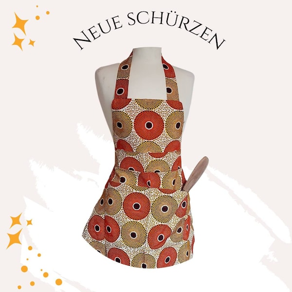 Puede incluir: Un delantal estampado en rojo, naranja y amarillo con un bolsillo grande y una cuchara de madera. El delantal tiene un estilo de cuello halter y está hecho de tela con un diseño geométrico.