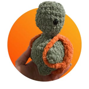 May include: A green crocheted stuffed toy with a large orange crocheted backpack. The toy has a round head and a small black eye.